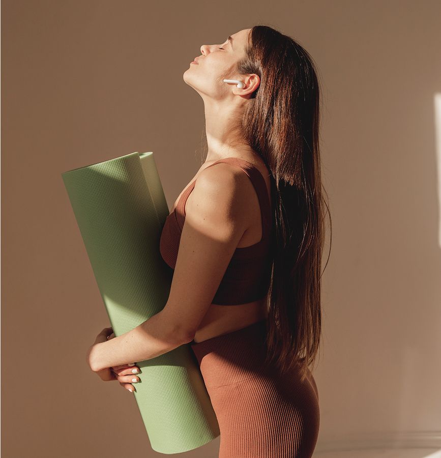 Woman holding yoga mat in sunlit space.