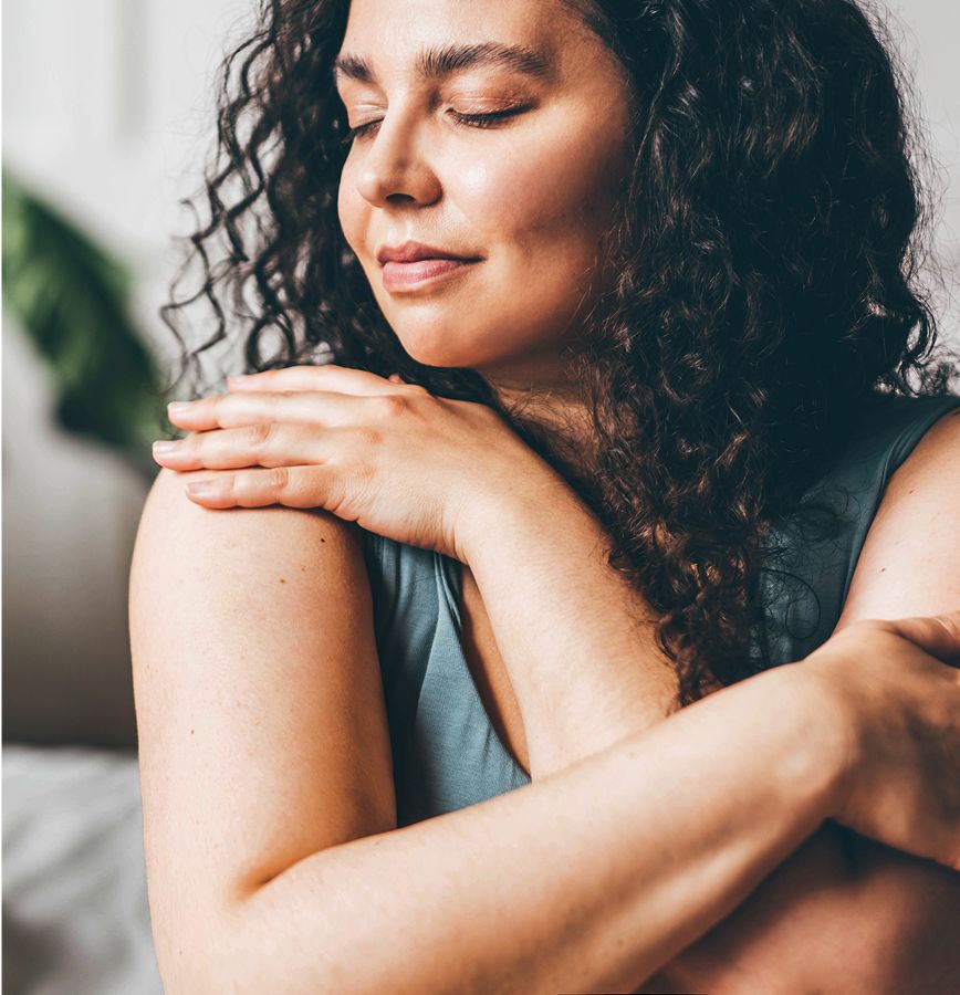 Woman with curly hair embracing herself gently.