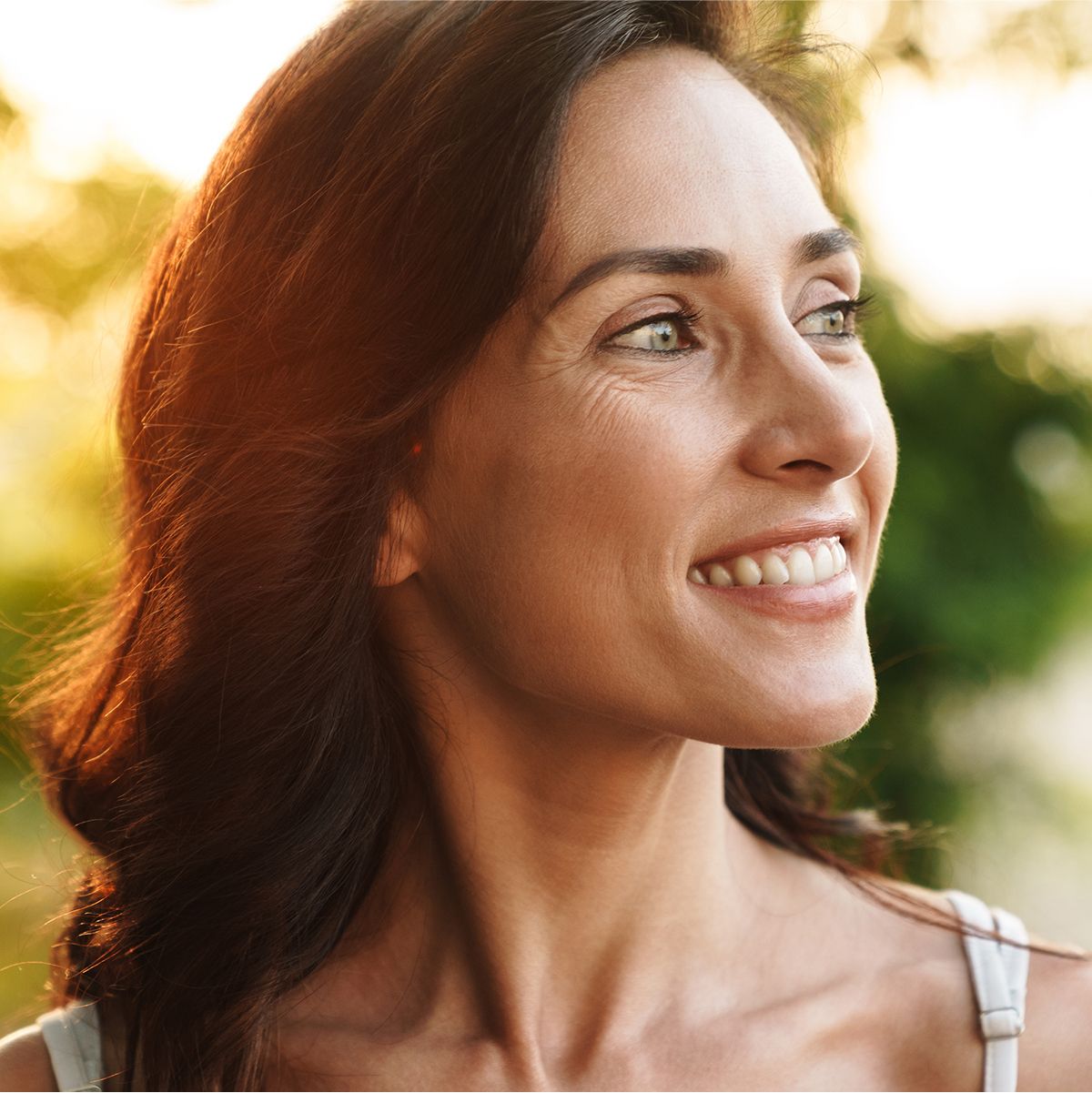 Smiling woman outdoors with natural sunlight background.