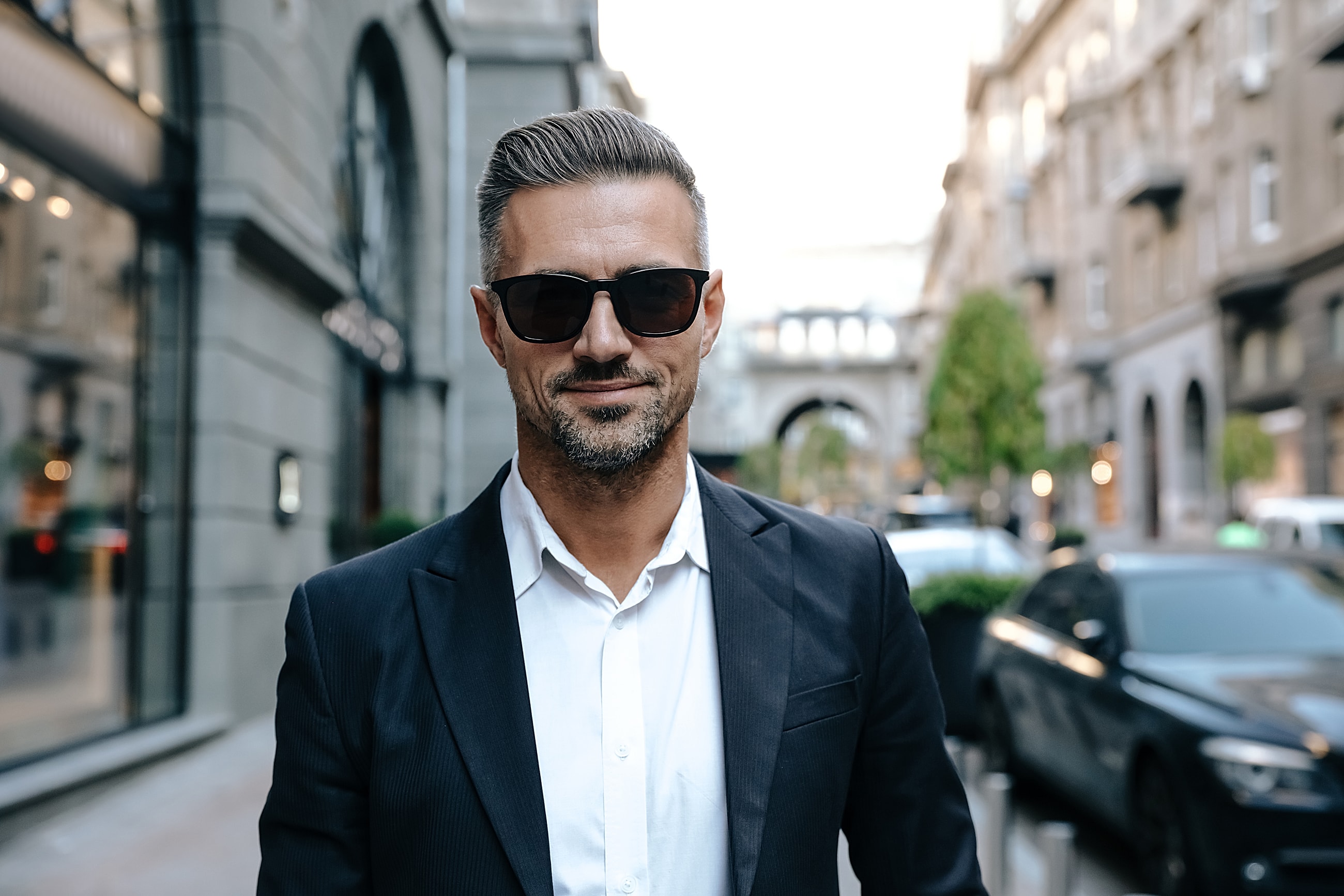 Stylish man in suit wearing sunglasses outdoors.